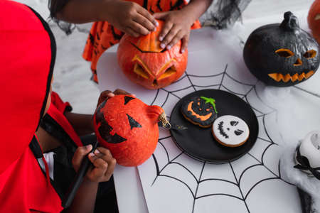 african american kid in halloween costume drawing on pumpkin near sisterの写真素材