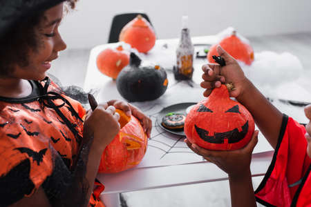 happy african american girl looking at drawing on pumpkin near brotherの写真素材