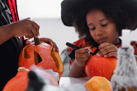 african american boy carving pumpkin while sister drawing on blurred backgroundの写真素材