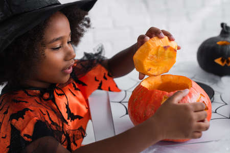african american girl in witch halloween costume carving pumpkinの写真素材