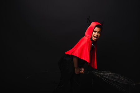 african american boy holding broom and screaming isolated on blackの写真素材