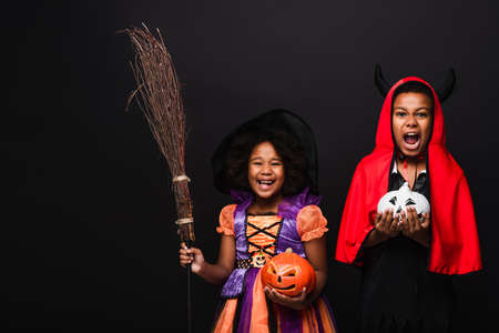 excited african american kids in halloween costumes holding carved pumpkins isolated on blackの写真素材