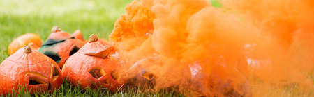 orange smoke near carved pumpkins on green lawn, bannerの写真素材