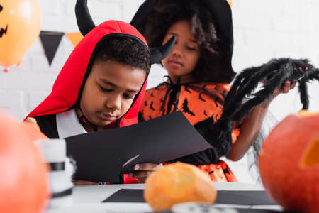 african american boy cutting black paper near sister in witch halloween costumeの写真素材