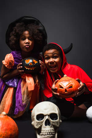 african american siblings in costumes holding creepy halloween pumpkins on blackの写真素材