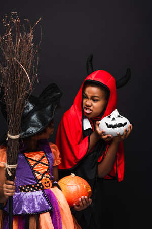 african american kids in halloween costumes holding creepy pumpkins isolated on blackの写真素材