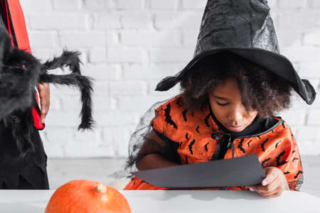 african american kid holding black paper near brother with toy spider