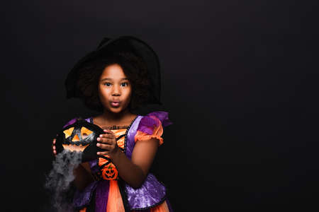 african american girl in halloween costume holding carved pumpkin isolated on blackの写真素材