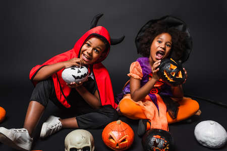 african american siblings in halloween costumes holding carved pumpkins on blackの写真素材