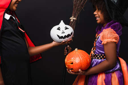 smiling african american kids in halloween costumes holding pumpkins isolated on blackの写真素材