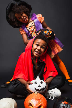african american children in halloween costumes holding carved pumpkins on blackの写真素材