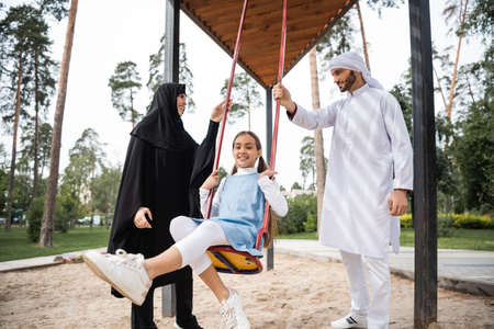 Smiling arabian child on swing near parents in park