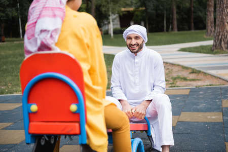 Happy arabian father in keffiyeh playing with son on playgroundの写真素材