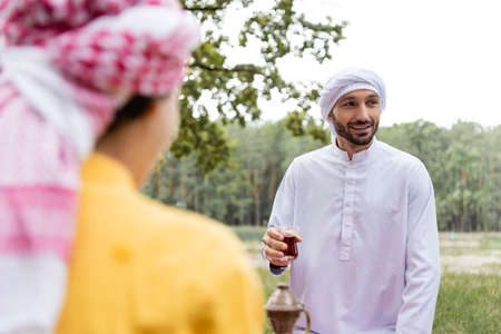 Smiling muslim man holding glass of tea near blurred son outdoorsの写真素材