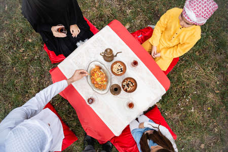 Top view of muslim family sitting near tea and food in park