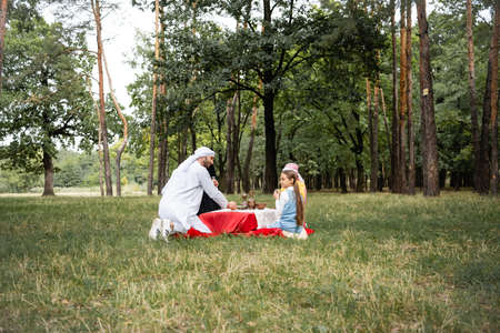 Positive arabian father sitting near family during picnic in parkの写真素材