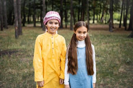 Muslim boy in kufiya smiling at camera near sister in park