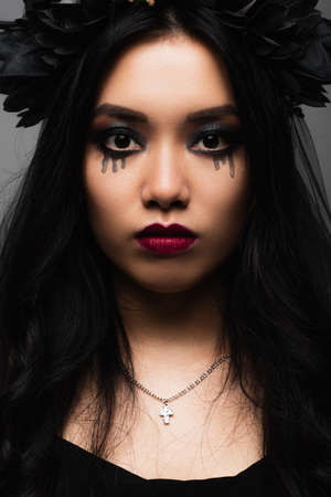 brunette asian woman with vampire halloween makeup looking at camera isolated on greyの写真素材
