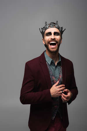 excited man in vampire king halloween crown laughing at camera isolated on greyの写真素材