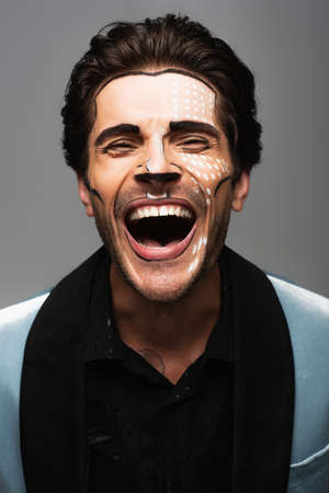 cheerful man in halloween makeup laughing at camera isolated on greyの写真素材