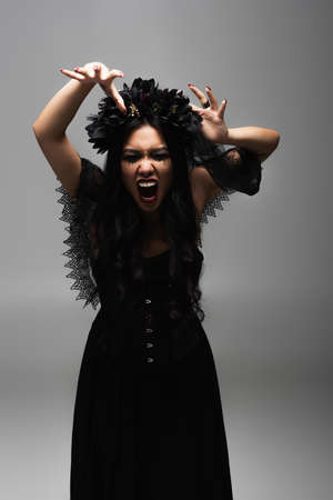 asian woman in vampire halloween costume showing scary gesture and growling isolated on grey