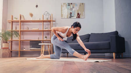 Brunette sportswoman stretching leg on fitness mat in living roomの写真素材