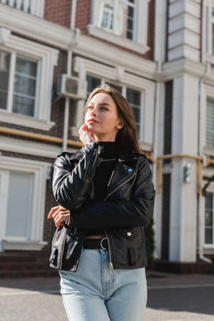 dreamy young woman in leather jacket standing on urban streetの写真素材