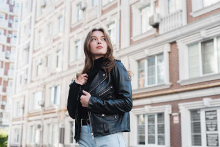 young woman in black turtleneck and leather jacket on urban street of europeの写真素材