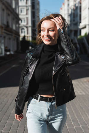 happy young woman in leather jacket standing on urban streetの写真素材