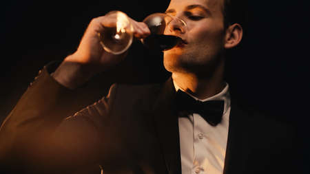 elegant man in suit drinking red wine isolated on blackの写真素材