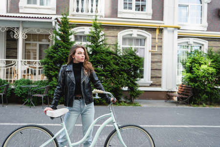 trendy young woman standing near bicycle on urban street of europe