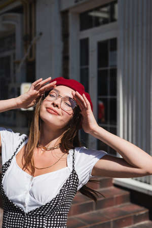 pleased young woman in red beret and eyeglasses enjoying sunlight