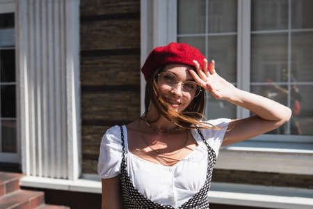 cheerful young woman in red beret and eyeglasses looking at camera