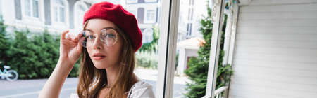 young woman in red beret adjusting eyeglasses and looking at camera, bannerの写真素材