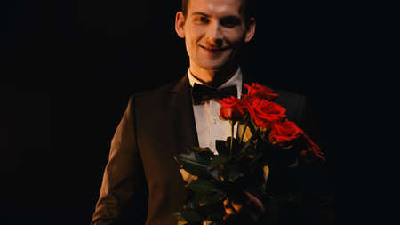 happy young man holding red roses and smiling isolated on blackの写真素材
