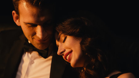 happy young woman smiling while leaning on shoulder of boyfriend isolated on blackの写真素材