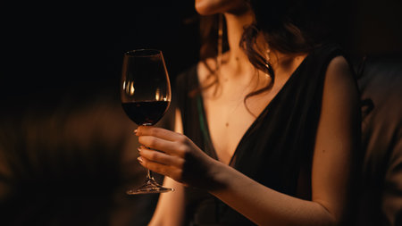 cropped view of elegant young woman holding glass of wine and sitting on sofa on blackの写真素材