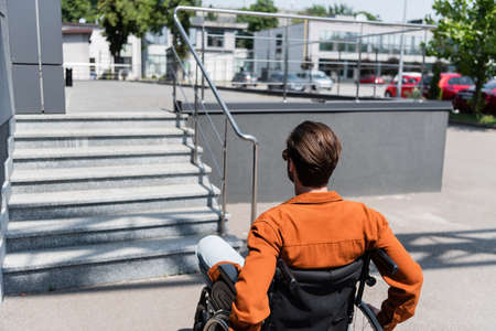 back view of young man in wheelchair near stairs on street