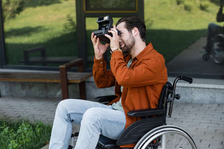 man in wheelchair taking picture on vintage camera outdoorsの写真素材