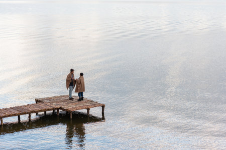 Multiethnic couple in blankets holding cups while talking on pierの写真素材