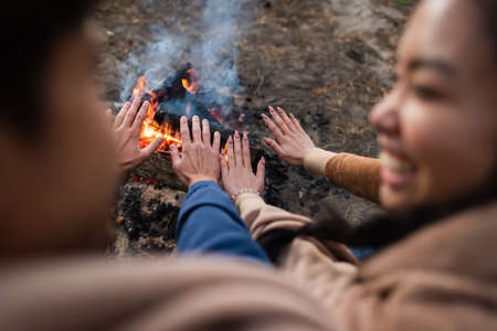 Blurred couple warming hands near campfire during weekend