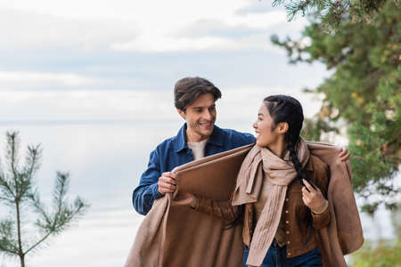 Man holding blanket near asian girlfriend with lake on background