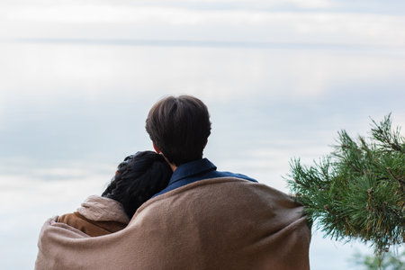Back view of couple in blanket standing near lake in autumnの写真素材