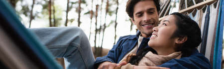 Smiling multiethnic couple resting in hammock in autumn, banner