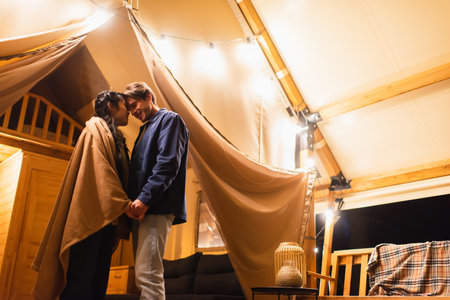 Happy interracial couple holding hands on glamping house terrace in eveningの写真素材