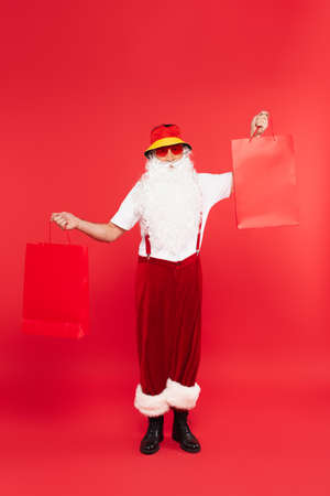 Santa claus in sunglasses holding shopping bags on red backgroundの写真素材