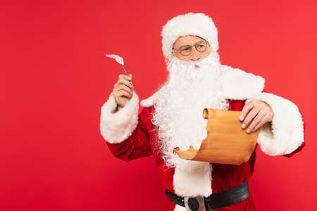 Thoughtful santa claus with pen and paper standing isolated on red