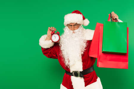 Santa claus in costume holding alarm clock and shopping bags isolated on greenの写真素材