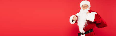 Santa claus holding sack and showing like isolated on red, bannerの写真素材