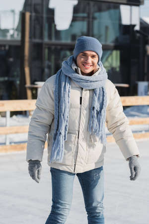 happy young man in scarf, winter hat and ice skates skating outsideの写真素材